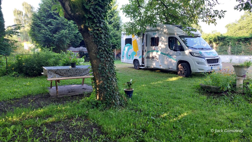 Un camping-car stationné près d'un arbre dans un jardin verdoyant avec une table et des plantes.